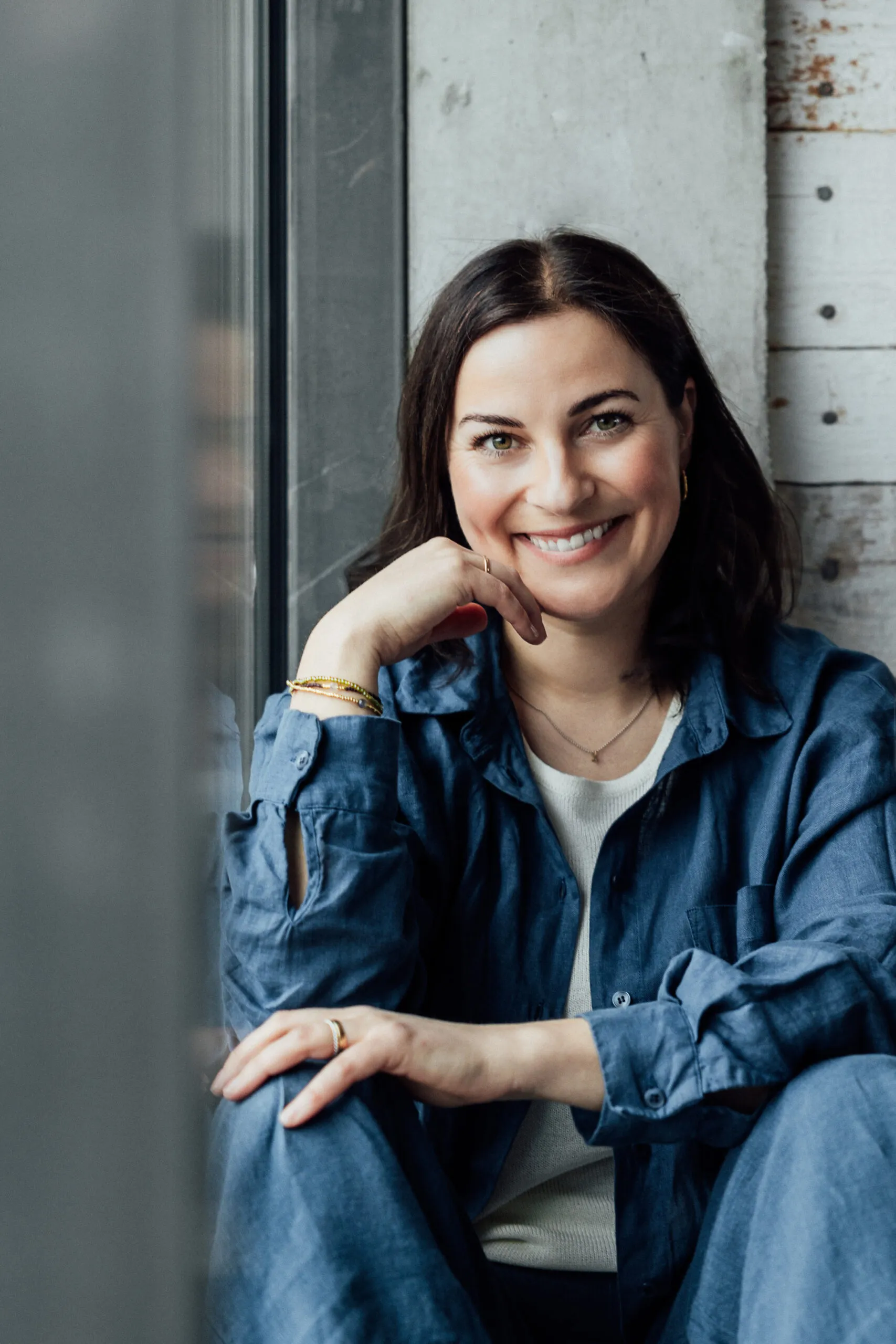 Julia Bechter sitzt am Fenster ihres Studios und lächelt direkt in die Kamera